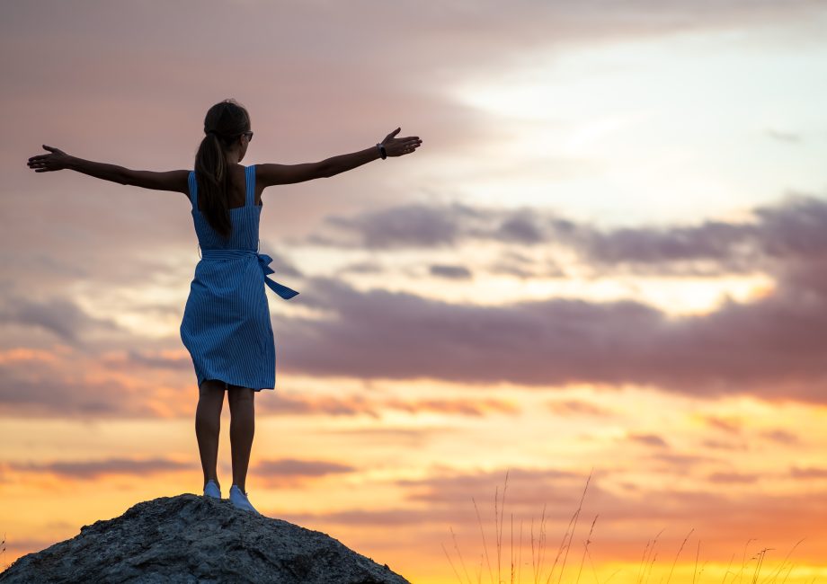 Silhouette d'une femme aux bras levés face au coucher du soleil, symbole de force et de liberté face aux féminicides en Belgique