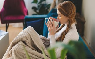 Femme enveloppée dans un plaid sur son canapé, une tasse de thé à la main : se préparer à l'heure d'hiver en douceur