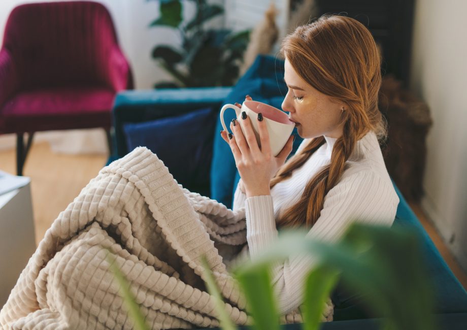 Femme enveloppée dans un plaid sur son canapé, une tasse de thé à la main : se préparer à l'heure d'hiver en douceur